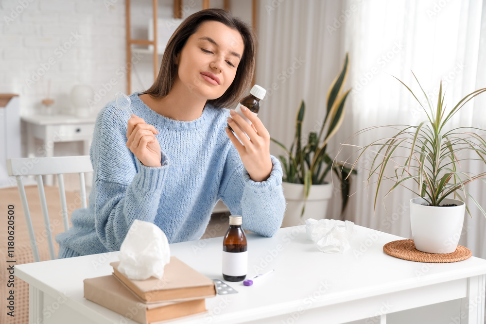 Sick young woman with cough syrup at table in bedroom Sick young woman with cough syrup at table in bedroom