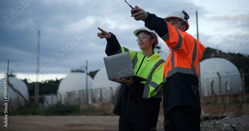 Male project engineers and female chemical engineers are engaged in a discussion regarding safety protocols in the chemical storage tank area at the oil refinery.