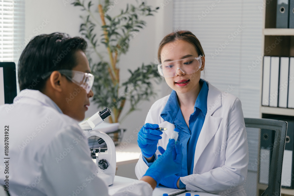 Two scientists wearing lab coats and safety glasses are examining a test tube containing a yellow liquid in a modern laboratory setting, with one scientist using a microscope Two scientists wearing lab coats and safety glasses are examining a test tube containing a yellow liquid in a modern laboratory setting, with one scientist using a microscope