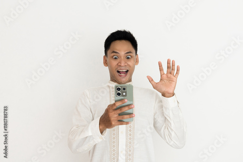 man wearing elegant traditional clothing looks excited while holding a smartphone, expressing amazement and curiosity at what he sees. photo