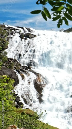 Kinsarvik, Hordaland, Norway. Waterfall Nyastolfossen In Hardangervidda Mountain Plateau. Nyastolsfossen in Spring Sunny Day. Height Of 115 m. Famous Natural Norwegian Landmark And Popular Destination photo