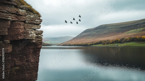 Dramatic cliff overlooking a serene lake with birds in flight, autumnal hues on distant hills. photo