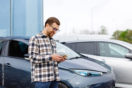 Young man holding money in hand standing front car and prepare pay by installments - insurance, loan and buying car concept insurance. Buy and down payment a car