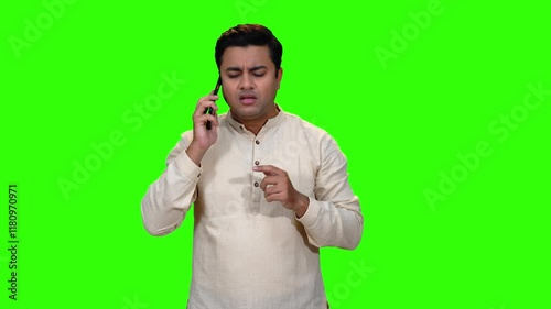 A young male model is chatting over his phone. He is looking for answers and is happy to get them. He is deeply engaged on his phone. A green screen studio.
