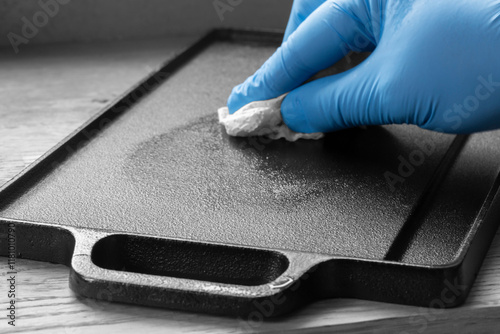 Person seasoning a cast iron plate with olive oil using a paper towel. On a wood background