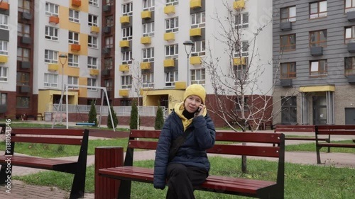 Woman talking on the phone on the street, person walking in an urban area, holding a mobile device for communication.