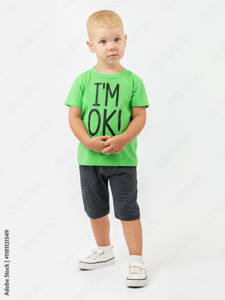 Surprised look, question. A 3-year-old blond boy in a T-shirt and shorts stands on a white background and looks expressively with his hands clasped. Surprised look, question. A 3-year-old blond boy in a T-shirt and shorts stands on a white background and looks expressively with his hands clasped.