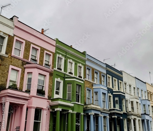 The iconic houses of Notting Hill stand proudly, showcasing vibrant pink, green, blue, and white facades under a cloudy sky, with no people in sight.