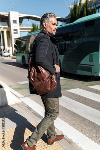 Active businessman with gray hair on crosswalk near public transport