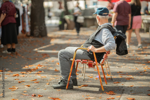 Obraz na płótnie Older unknown person sitting in a chair and enjoying the hustle of an open street market. Elder person relaxing in an old colorful beaten up chair. w salonie
