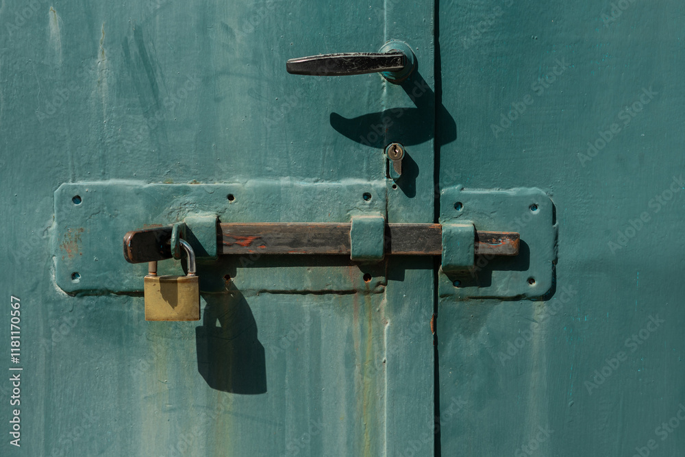 Old metal door with hook, lock and latch, secured with a golden padlock. Worn door with traces of rust and thick crusty layer of paint