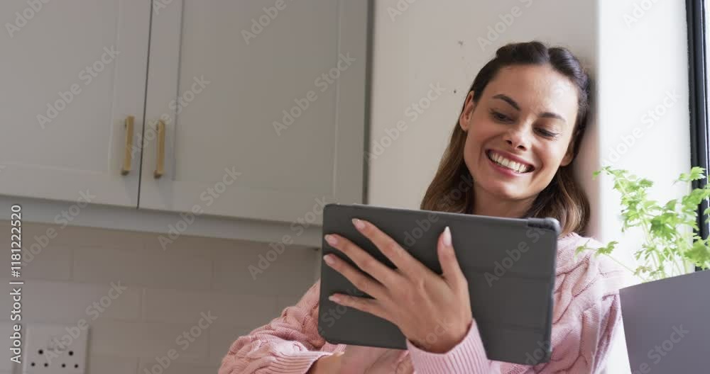 At home, woman in pink sweater smiling while using tablet near window, copy space At home, woman in pink sweater smiling while using tablet near window, copy space