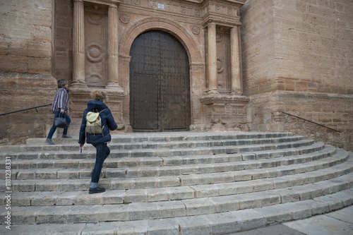 Two friends ascending the stone steps of a majestic church during a cultural exploration in a Spanish town, admiring its grand historic entrance and classical architecture