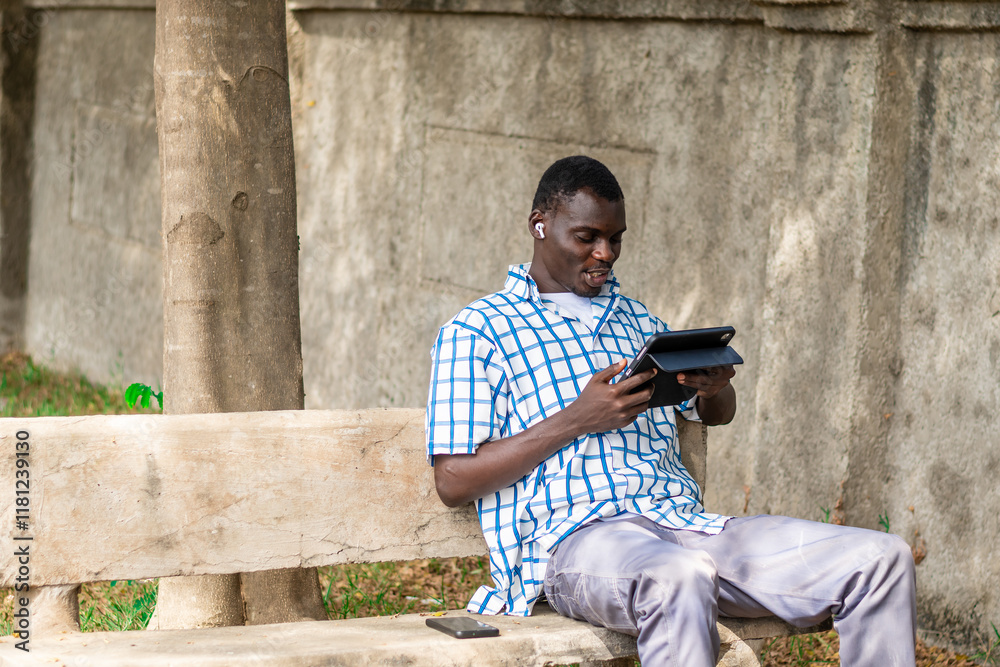 Obraz premium African American man seated in the garden calmly using phone for leisure, Technology, game, gamer, gaming, connection