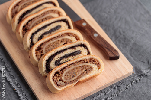 Bejgli, home-baked roll, traditional Hungarian, Eastern European Christmas and Easter sweet bread in slices stuffed with ground walnuts and poppy seed filling on wooden cut board on a gray background photo