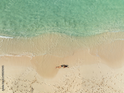 Aerial view of a woman relaxing on a beautiful beach with turquoise clear water and soft sand, North Eleuthera, The Bahamas. photo