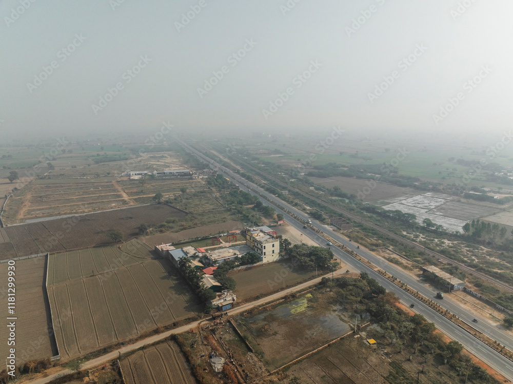 Aerial view of rural farmland and highway with scattered buildings under a hazy sky, Bharhkol, Uttar Pradesh, India. Aerial view of rural farmland and highway with scattered buildings under a hazy sky, Bharhkol, Uttar Pradesh, India.