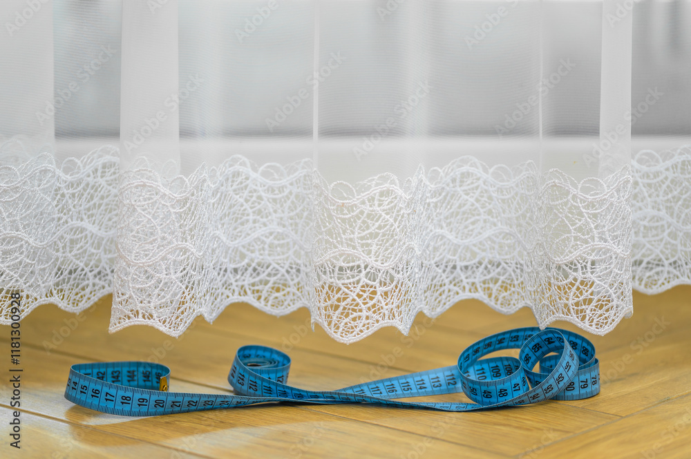 Obraz premium Centymetr krawiecki leżący obok wiszącej w oknie firance, 
