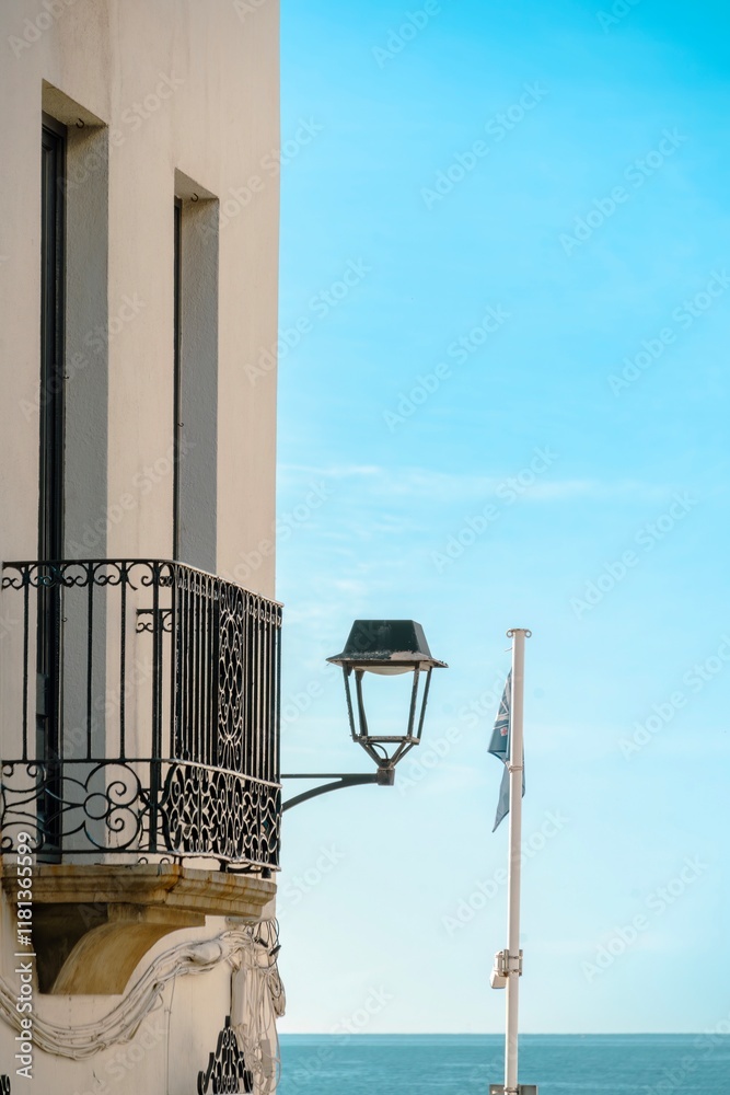 A lamp post with a blue flag on top of it. The lamp post is on a balcony overlooking the ocean