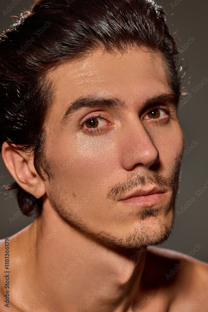 Fototapeta premium Close-up of man with neutral expression gazing slightly off-camera against dark background. Male model with slicked-back hair and sharp facial features. Concept of male beauty and facial care,