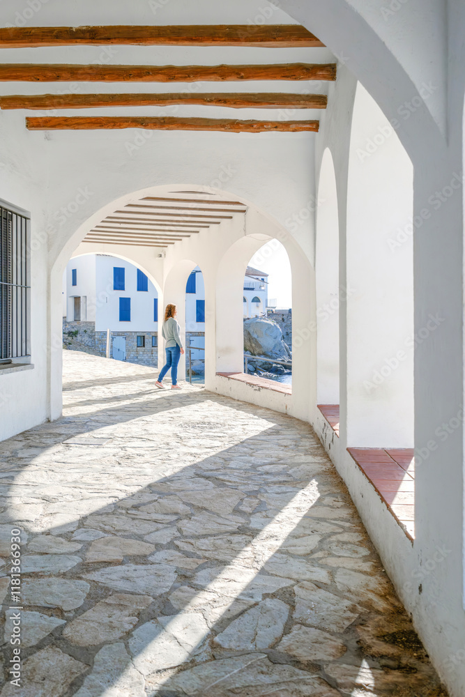 A Tourist Girl Looking Through Of The Arches Of The Promenade Of The Tourist City Of Calella De Palafrugell, Costa Brava, Catalonia. Scenic fisherman village with nice sand beach and clear blue water