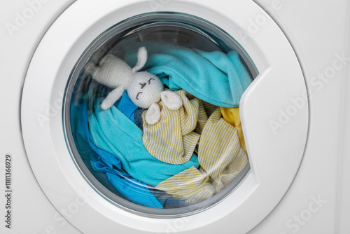 Washing machine with clothes and toy bunny as background, closeup