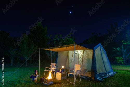 Camping tents at night, vintage cabin tents, antique gas lamps, retro chairs, and a group of camping tents with outdoor coffee-making facilities on  tables in a forest camping area in the forest
