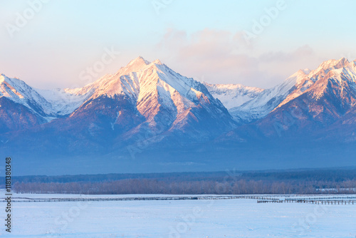 Winter landscape of snow-covered field of foothill Tunka valley with snowy Eastern Sayan Mountains at sunset. Natural background. Winter travel. Siberia. Baikal region. Buryatia. Tunkinsky Nature Park photo