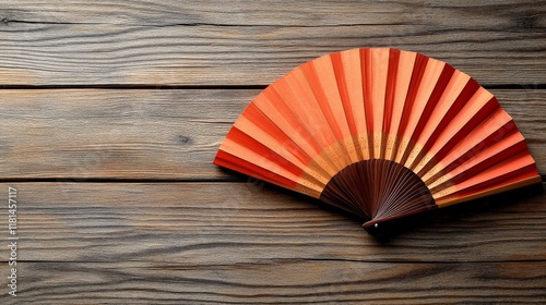 Decorative hand fan with orange and red hues placed on a wooden surface