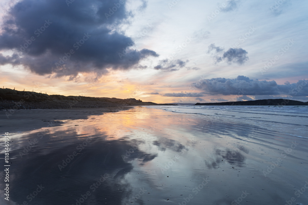 Obraz premium Sur la plage de l'Aber, un lever de soleil avec un ciel bleu clair et un jaune pâle, où quelques nuages gris se reflètent sur le sable mouillé, créant une ambiance douce et apaisante.