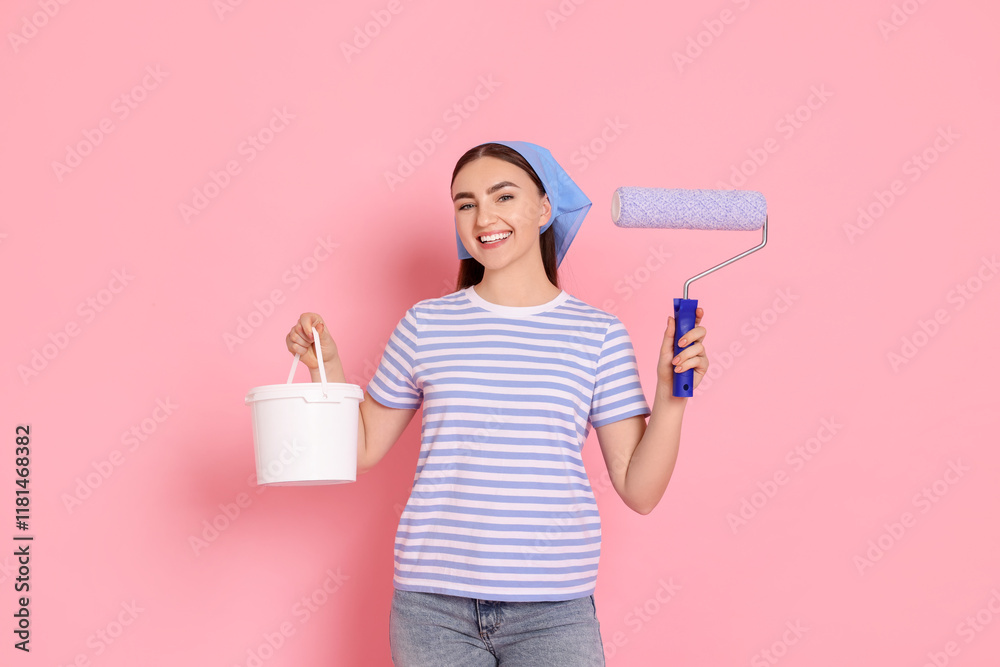Portrait of young decorator with paint roller and bucket on pink background Portrait of young decorator with paint roller and bucket on pink background