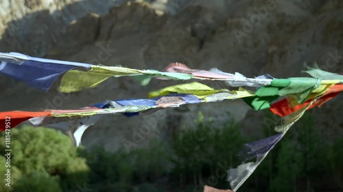 Colorful prayer flags blowing in the wind in a mountainous outdoor setting - slow motion pan across vivid multi coloured Tibetan Buddhist flags flying in remote Himalayas region of Ladakh