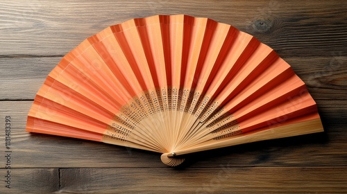 Decorative hand fan with orange and red hues placed on a wooden surface