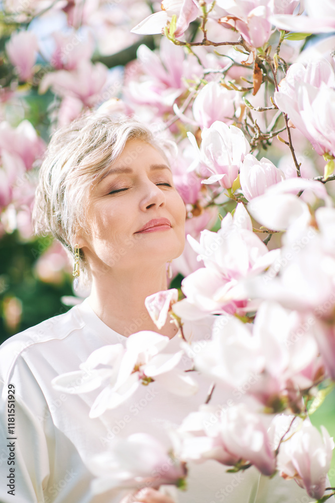 Spring close up portrait of beautiful 55 - 60 year old woman posing with magnolia tree Spring close up portrait of beautiful 55 - 60 year old woman posing with magnolia tree