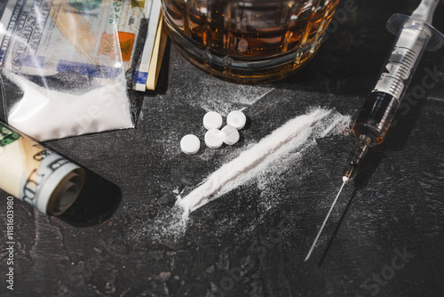 White narcotic pills, an alcoholic drink in a glass, a syringe with a dose of heroin, a line of cocaine powder and US dollar bills on a dark background. Concept of addiction and bad habits