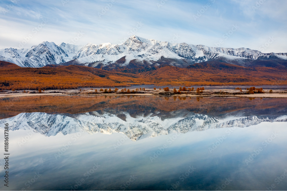 Obraz premium Scenic view of snow-covered mountains mirrored in calm lake surrounded by autumn forest in Altai.