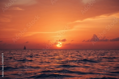 Vibrant orange sunset over calm ocean with a sailboat photo