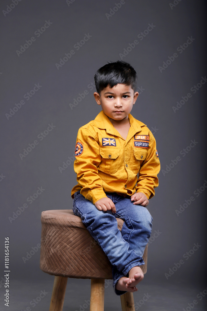 A Small Boy Sitting On A Stool Is Posing A Small Boy Sitting On A Stool Is Posing