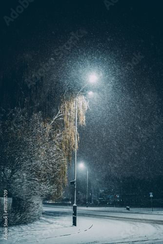 Snowfall at night under a streetlight, creating a peaceful winter atmosphere. Ideal for winter-themed designs, urban landscapes, or serene seasonal visuals. photo