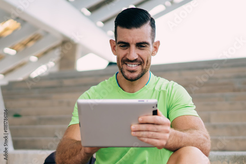 Cheerful male in sportswear using digital tablet for browsing wireless information about workout training, happy Caucaisan athlete enjoying online messaging in social networks using touch pad photo