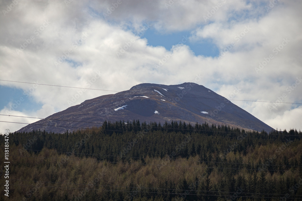 Majestic Scottish mountain landscape with snow-capped peak and lush green forest under a cloudy sky Majestic Scottish mountain landscape with snow-capped peak and lush green forest under a cloudy sky