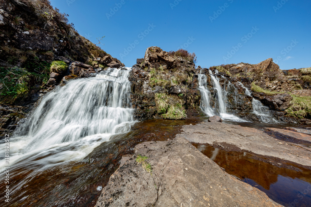 Waterfalls cascading over rocky terrain in the Isle of Skye, Scotland, under a clear blue sky during daytime Waterfalls cascading over rocky terrain in the Isle of Skye, Scotland, under a clear blue sky during daytime