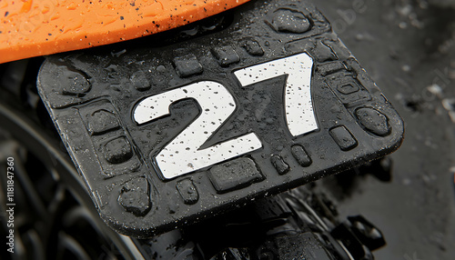 Close-up of a wet number 27 plate on a motorbike fender, showcasing texture and raindrops.
