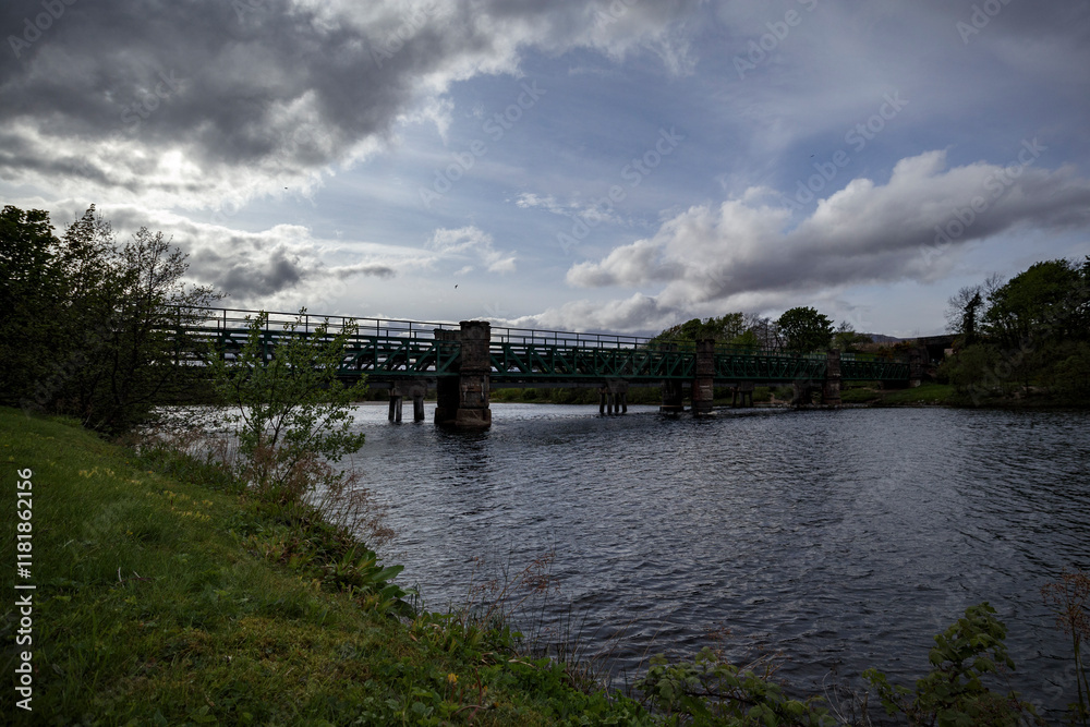 Fototapeta premium Bridge spanning a serene river in the lush landscape of Scotland during a cloudy afternoon