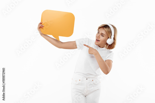 Young blonde woman listening music in headphones over red background. Woman pointing finger on blank speech bubble. photo