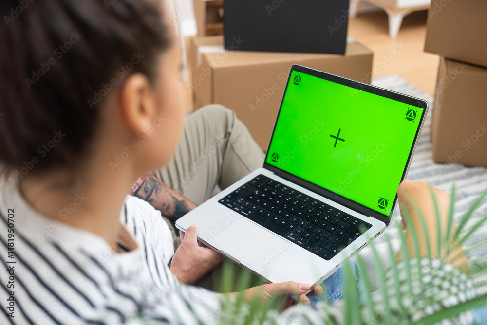 laptop with an empty green mock-up screen, held amidst cardboard boxes, signifies a young couple's move to their new living space laptop with an empty green mock-up screen, held amidst cardboard boxes, signifies a young couple's move to their new living space