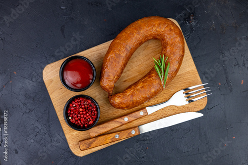 Delicious smoked sausage served on a wooden platter with spicy ketchup and pink peppercorns, perfect for a gourmet meal at any time