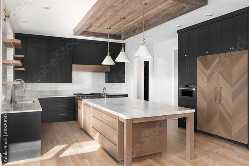 A luxury black detail kitchen with pendant lights and wood frame over a large island, stainless steel appliances, white tiled backsplash, and a white oak wood panel refrigerator. No brands or labels. photo