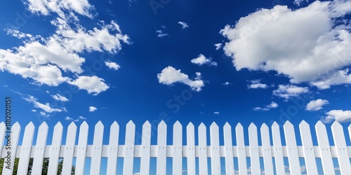 A white fence made of pickets stands out prominently against a bright blue sky backdrop, creating a picturesque scene that emphasizes the charm of the setting. photo