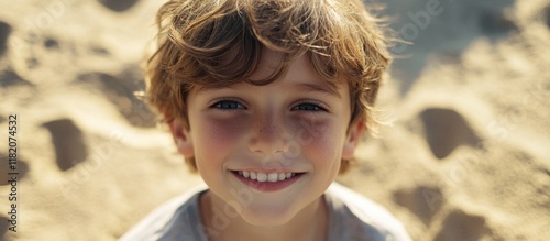 Happy young boy with curly hair smiling joyfully on a sandy beach, bright sunlight illuminating his face, shallow depth of field. photo